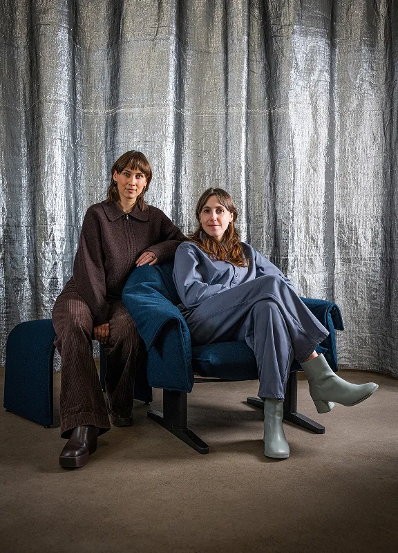 Zwei Frauen sitzen entspannt im petrolfarbenen Loungechair Bascule vor einem silbernen Vorhang.