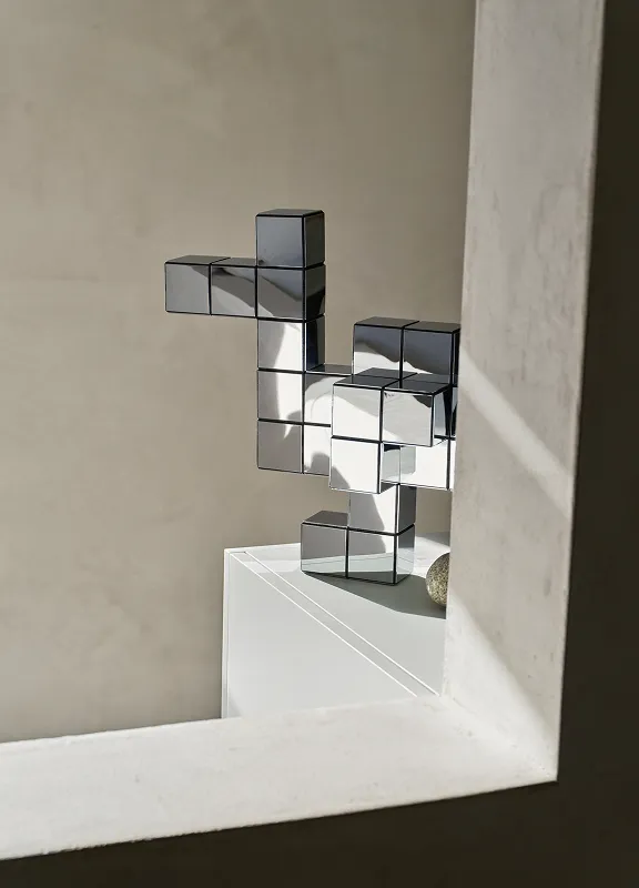 Eine spiegelnde schwarze Panton-Cubes-Skulptur steht auf einer Fensterbank im Sonnenlicht.